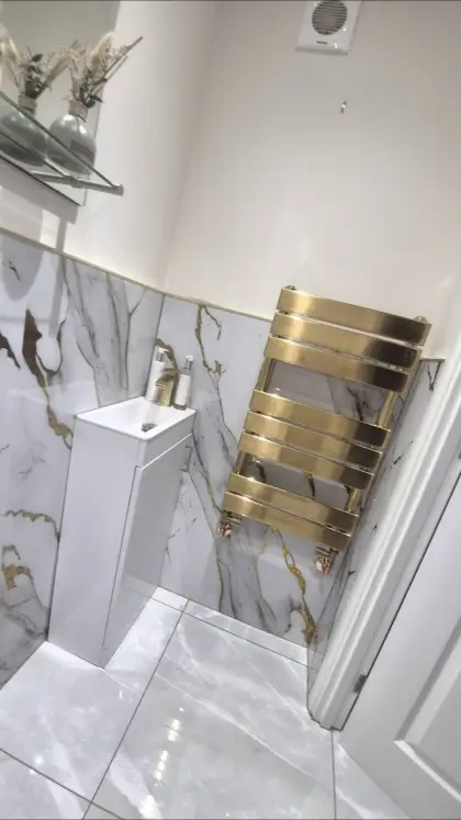 Brushed brass towel radiator in a marble-effect cloakroom